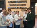 Uczniowie trzymający prezenty wraz z Panem Pawłem Lisiakiem stoją w holu i uśmiechają się