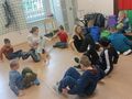 2. Uczniowie siedzą na podłodze na sali gimnastycznej i naśladują bąka.