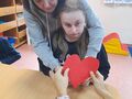 Dziewczynka przekłuwa szpilką papierowe serce z pomocą nauczycielki