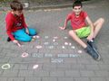4 Uczniowie trzymają kolorowe kredy rysują kółka na kostce brukowejjpg