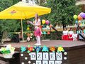 Uczennica znajduje się na scenie na dworze czyta przemowę. Scena jest udekorowana kwiatami i balonami oraz napisem Dzień Taty. W tle widać drze