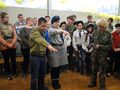 Dwoje harcerzy ubrani w mundury harcerskie stoją z uniesioną prawą ręką składają przysięgę harcerska w tle znajduje się grupa innych harcerzy