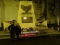 Harcerz z druhną stoją przed Pomnikiem Powstańców Wielkopolskich harcerz tzyma na ramieniu flagę Polski jest ciemno przed pomnikiem widać palące się znicze w biało czerwonych barwach