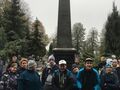 Harcerze i uczniowie znajdują się na cmentarzu stoją w grupie przed pomnikiem ku czci poległym żołnierzom w tle widać drzewa