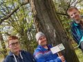 Trzech chłopców stoi przed drzewem jeden z nich trzyma tabliczkę z napisem kasztanowiec 