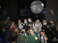 7. Uczniowie wraz z opiekunami pozują do zdjęcia grupowego na tle ogromnej kuli ziemskiej. Wszyscy uśmiechają się i unoszą kciuki w górę 