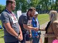 5. Uczniowie stoją na podium na szyi mają zawieszone medale. Kobieta im gratuluje 