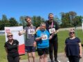 7. Uczniowie stoją na podium mają na szyi medale. Obok dwie kobiety w tle boisko do piłki nożnej 