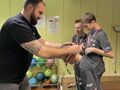 6. Trzech uczniów stoi obok siebie na szyi mają zawieszone medale. Przed nimi nauczyciel wręcza uczniowi medal 