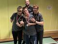 7. Trzech uczniów stoi obok siebie uśmiechają się mają zawieszone na szyi medale. Za nimi nauczyciel 