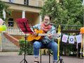 2. Dziewczyn siedzi na krześle na scenie gra na gitarze i śpiewa do mikrofonu 