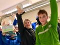 Uczniowie się cieszą i unoszą rece do góry. Chłopiec trzyma statuetkę