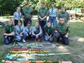Druhnyi druhowie pozują w dwóch rzędach do zdjęcia grupowego. Znajdują się w otoczeniu parku przed nimi znajduje się ułożone z rozsypanki wyraz