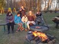 grupa wychowawnków siedzi na ławce wraz z opiekunem przed nimi pali się ognisko