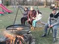 grupa wychowawnków siedzi na ławce wraz z opiekunką przed nimi pali się ognisko