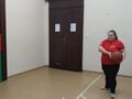 1. uczennica rzuca piłkę koszykową do celu, trzyma piłkę w rękach, stoi w wyznaczonej na podłodze strefie z taśmy klejącej