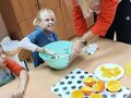 2. Dziewczynka z pomocą nauczyciela miesza smalec z ziarnami