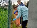 7 uczennica zbiera śmieci przy płocie z pomocą nauczycielki