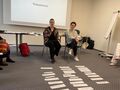 2. Dwie tutorki siedzą na krzesłach przed nimi leżą na podłodze kartki w tle ekran 