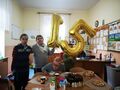 4 Jubilat siedzi przy stole a obok niego stoją chłopcy i trzymają balony 