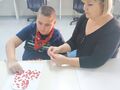 4 uczeń tworzy kartkę z pomocą nauczyciela siedząc przy stole w bibliotece
