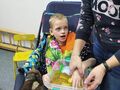 Zwiększanie pola doświadczeń dotykowych Uczestnik zajęć zespołowych siedzi w wózku opiekun dostarcza wrażeń dotykowych zanużajac jego rękę w materiale sypkimjpeg