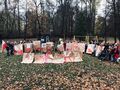Uczniowie tworzą napis na placu zabaw Niepodległa Polska. Na szarym papierze każda litera jest na pojedyńczym arkuszu. Cała grupa uczniów wraz z nauczycielami trzyma ułożony napis