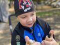 Chłopiec siedzi na dworze w rękach trzyma cylindry naciskowe Montessori. Uczeń rozpoznaje stopień oporu podczas nacisku. Zestawia je w identycz