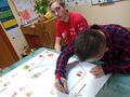 Dwóch uczniów znajduje się w klasie siedzą przy ławce jeden z nichrysuje markerem linie na dużym arkuszu papieru 