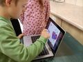 chłopiec rozwiązuje zadanie na laptopie przy stoliku obok kibicuje mu dziewczynka
