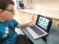 chłopiec siedzi przy stole i rozwiązuje zadanie na laptopie w tle drukuje drukarka 3d