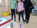 dziewczynka wspomagana przez nauczyciela steruje zadlnie sterowanym robotem z klocków lego obok stoi chłopiec