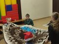 7.Dzieci siedzą na podłodze i trzymają koc za rogi z kulkami