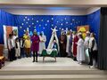 8.jasełka występ uczniów uczniowie i nauczyciele przebrani za aniołów pasterzy królów Józefa i Maryję stoją na scenie pani prowadząca mówi do mikrofonu przemawia
