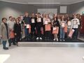 Liczna grupa uczniów wraz z nauczycielami pozują do zdjęcia na scenie. Uczniowie trzymają dyplomy puchary i nagrody 