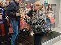 Nauczyciel składa uczniowi gratulacje oraz wręcza mu dyplom i puchar. Uczeń znajduje się na scenie w tle widać stojących innych uczniów 