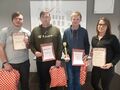 Trzech uczniów i nauczycielka stoją w rzędzie pozując do zdjęcia. Trzymają w rękach dyplomy puchar i nagrody 