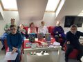 Uczestnicy konkursu siedzą na czerwonej kanapie i na czerwonych pufach 