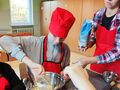 chłopiec wsypuje mąkę do miski z pomocą nauczycielki