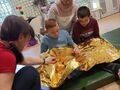 uczniowie dotykaja foli aluminiowej, siedzą na materacu
