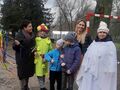 Uczniowie z dorosłymi pozują do zdjęcia z uczennicami przebranymi za Panią Wiosnę i Panią Zimę. Znajdują się w parku 