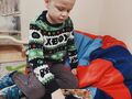 Chłopiec siedzi na dywanie i otwiera prezentjpg
