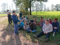 Odpoczynek Uczestnicy wraz z opiekunami siedzą na trawie w zacienionym miejscu 