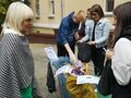 Grupa osób znajduje się przed budynkiem szkoły. Dwie osoby rozmawiają ze sobąpozostałe dwie segregują śmieci do worków odpowiedniego koloru 