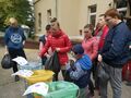 Uczniowie mają założone rękawiczki trzymają worki ze śmieciami segregują je do worków odpowiedniego koloru. Znadują się przed budynkiem szkoły