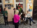 Pani Dyrektor trzyma mikrofon z tyłu na ławce siedzi rodzice z dzieckiem obok stoją nauczyciele