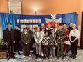 grupa teatralna uczniów ustawiona do zdjęcia grupowego na tle niebieskim z napisem Narodowe Święto Niepodległości i biało czerwoną flagą