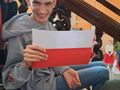 Zdjęcie przedstawia uśmięchniętego chłopca trzymającego w ręce polską flagę 