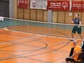 zawodnicy grają w badmintona obok stoi sędzia oraz wolonariusze siedzą przy stole i zapisują punkty