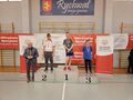 zawodnicy stoją na podium obok stoi pan w garniturze